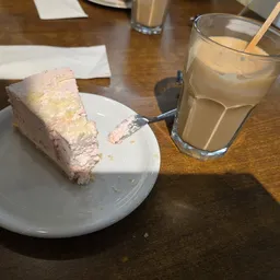 Bord met stuk cake en glas met bruin drankje op houten tafel in lunchroom