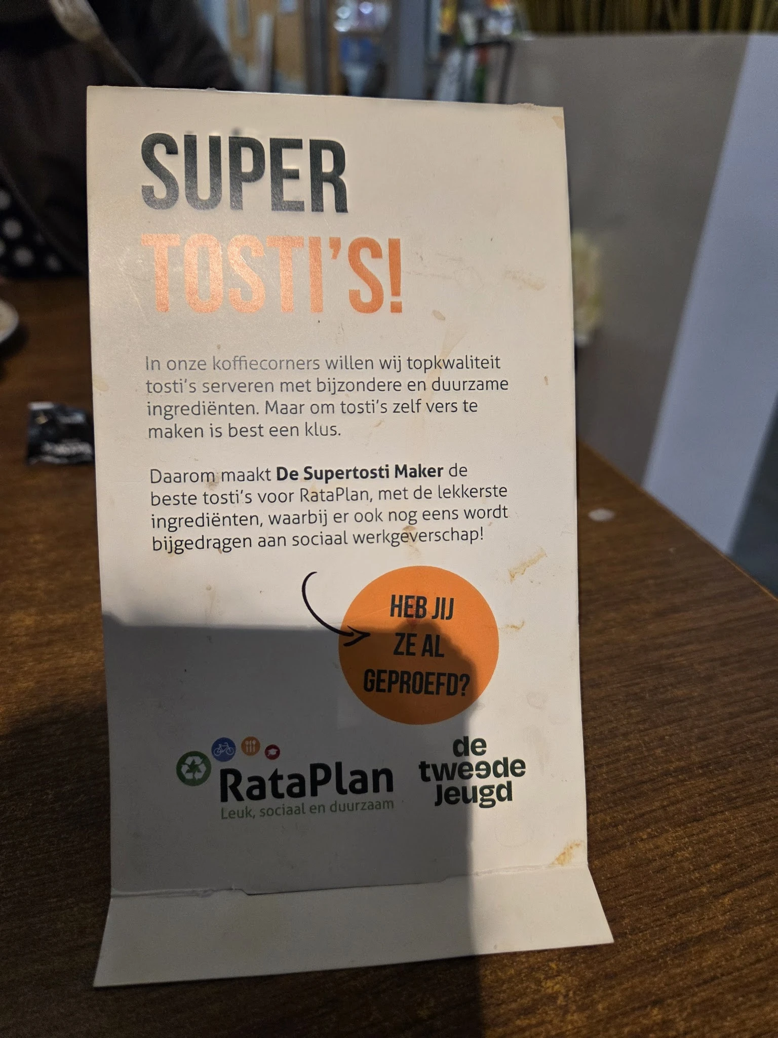 Informatieposter over tosti's in de koffihoek van de kringloopwinkel met tekst over ingrediënten en een vraag om feedback