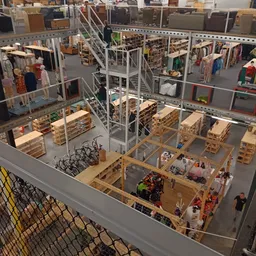 Overzicht van de kringloopwinkel met stellingen, kleding aan rekken, houten pallets en werknemers op de werkvloer