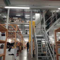 Ruim winkelinterieur met houten stellingen, metalen trappen en galerijen, winkeliers en bezoekers tussen de uitstalkanten