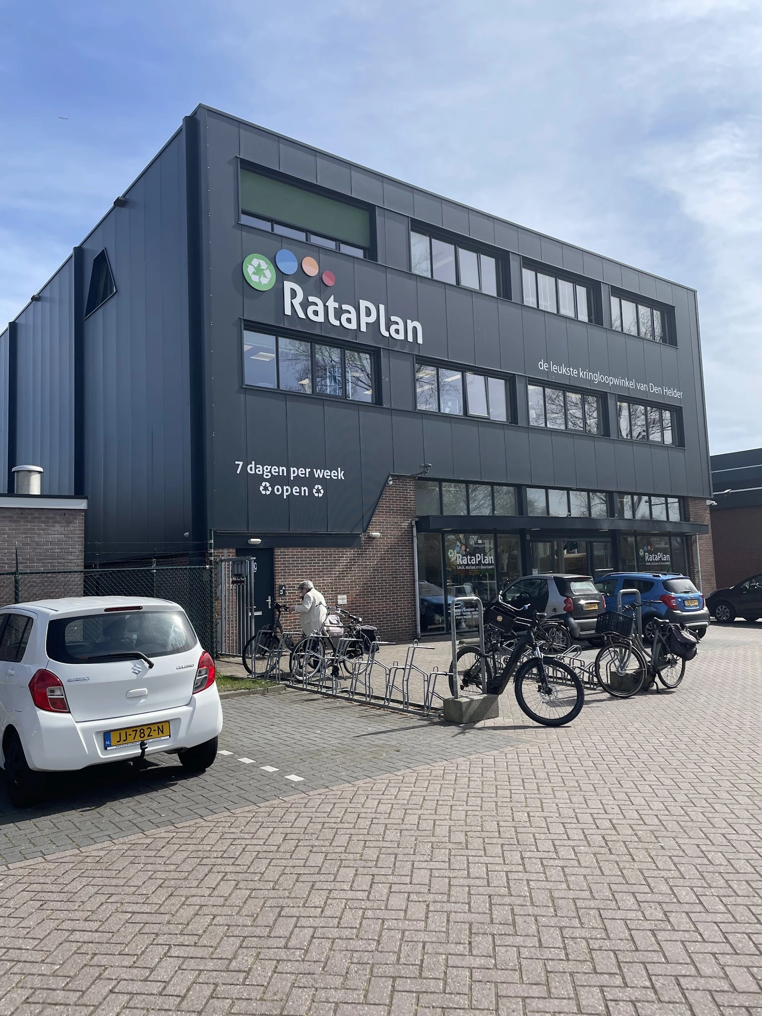 Voorgevel van RataPlan kringloopwinkel met donkere gevel, grote ramen, winkelentree en fietsenstalling met fietsen