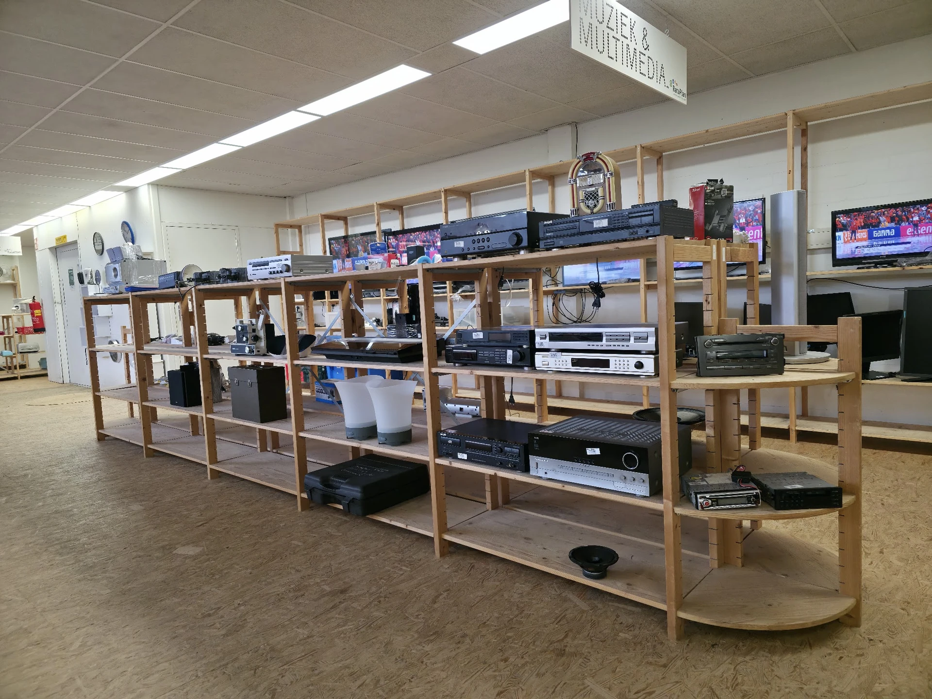 Houten stellingsysteem met audiovisuele apparatuur, televisies en elektronische items in kringloopwinkel