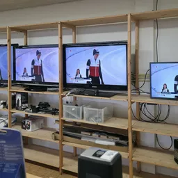 Houten stellingkasten met televisies waarop een presentator wordt getoond, met opbergdozen en spullen op de planken