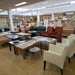 Winkelvloer met meubels uitgestald: witte fauteuils, bruine banken, houten tafels en andere meubels in een ruime ruimte met h