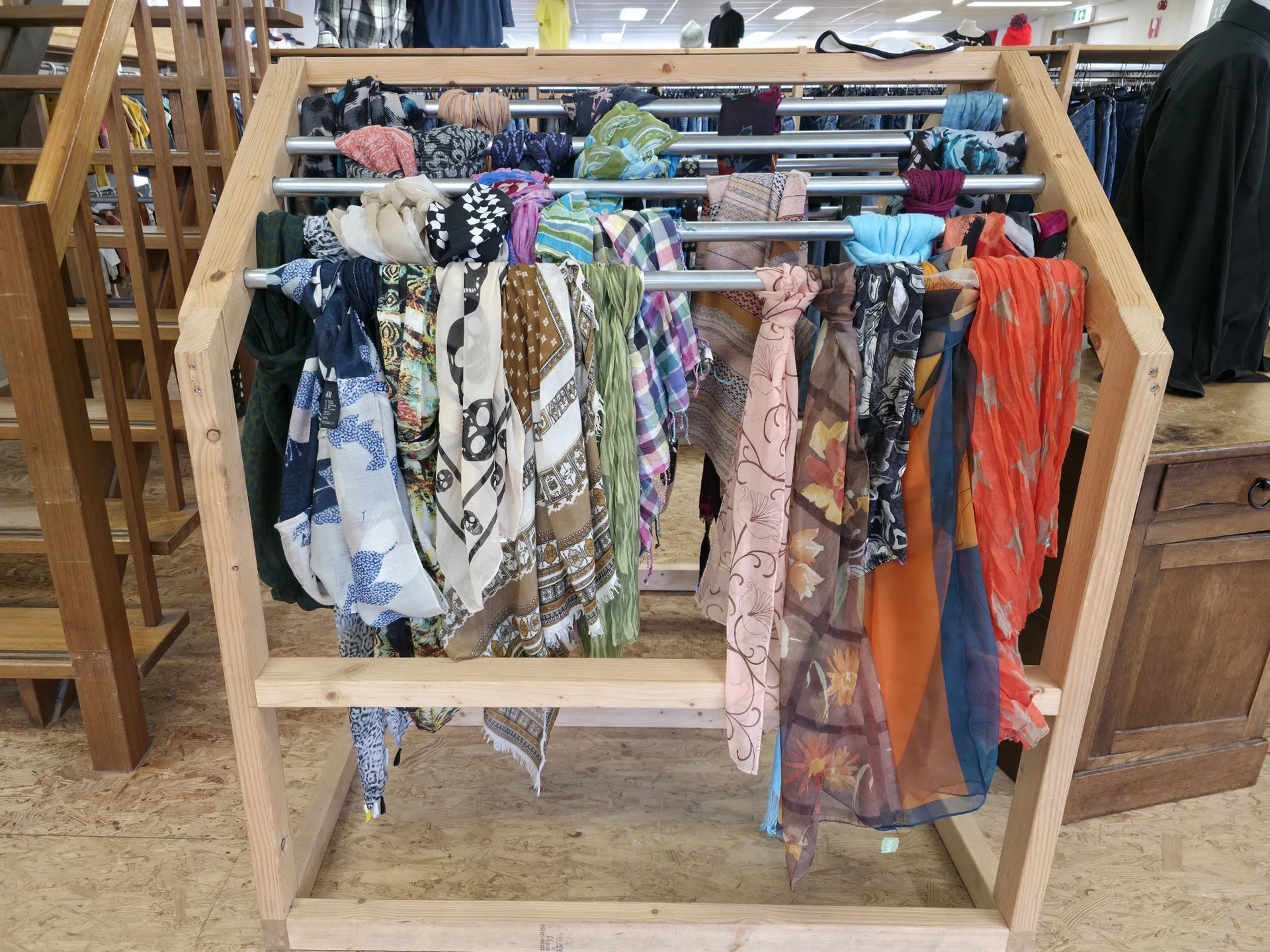 Houten rek met kleurige tweedehands kleding en textiel uitgestald op hangers