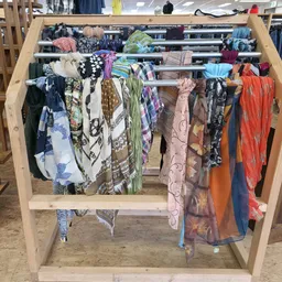 Houten rek met kleurige tweedehands kleding en textiel uitgestald op hangers