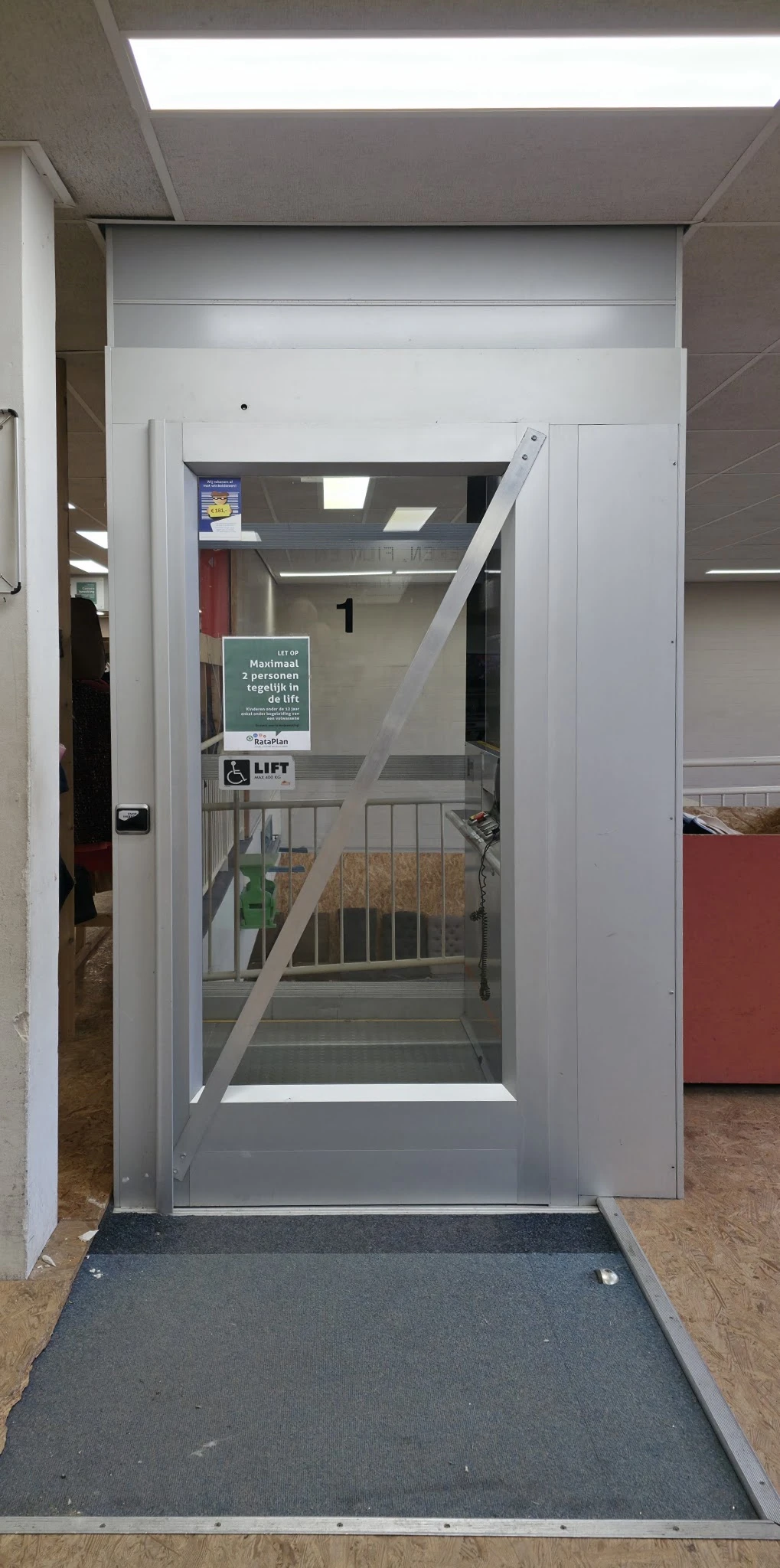 Trappenhuiszone met lift en waarschuwingsbord voor maximaal 2 personen in kringloopwinkel