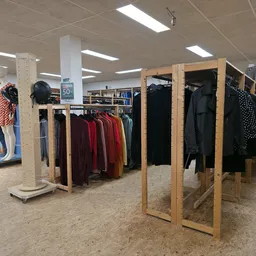 Winkelvloer met houten rekken vol tweedehands kleding, stellingen op de achtergrond en fluorescerende plafondverlichting