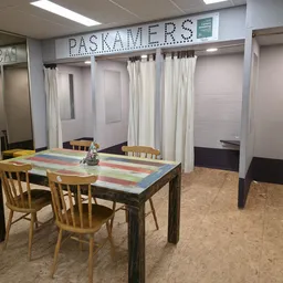 Winkelvloer met houten tafel, stoelen, gordijnen en winkelrekken met het opschrift 'PASKAMERS'