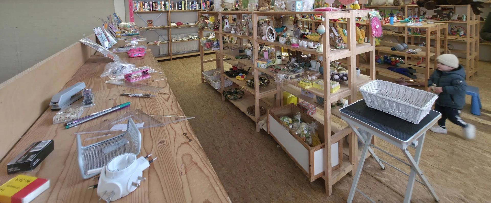 Winkelvloer met houten stellingen vol spullen, roze bakken en diverse tweedehands artikelen