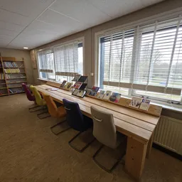 Bibliotheekachtig interieur met werkplekken aan raam, boekenkast en shutters