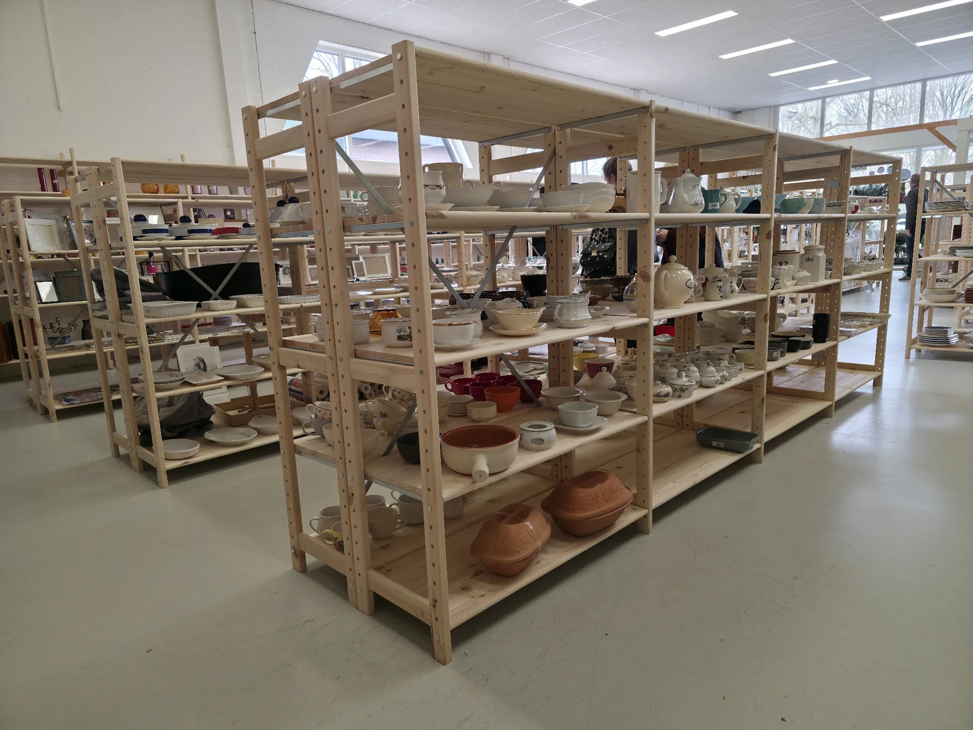 Houten stellingen met diverse huishoudelijke artikelen, servies en keramiek in een kringloopwinkel