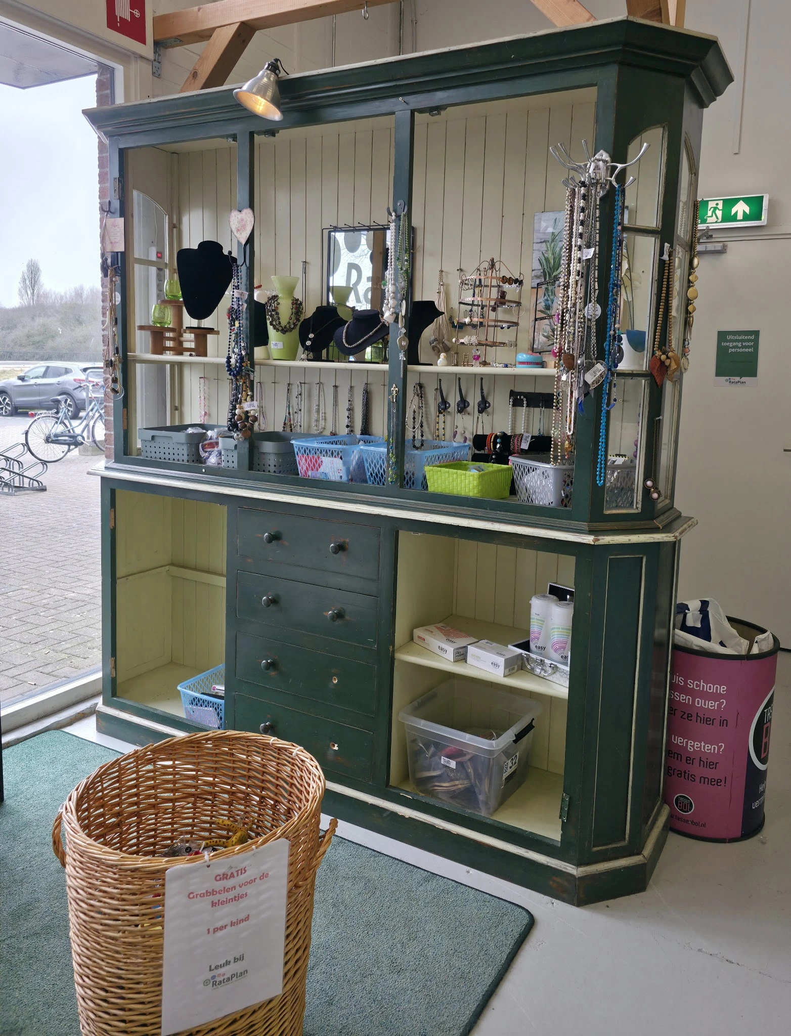 Groen meubelstuk met spiegels, sieraden en accessoires op display, met open kasten en laden vol opgestelde items