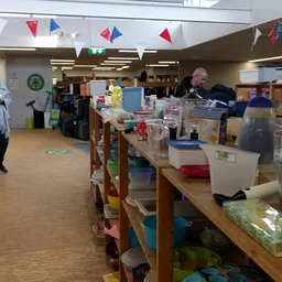 Winkelvloer met tafels vol plastic bakken, dozen en spullen, personeel aan het werk op achtergrond