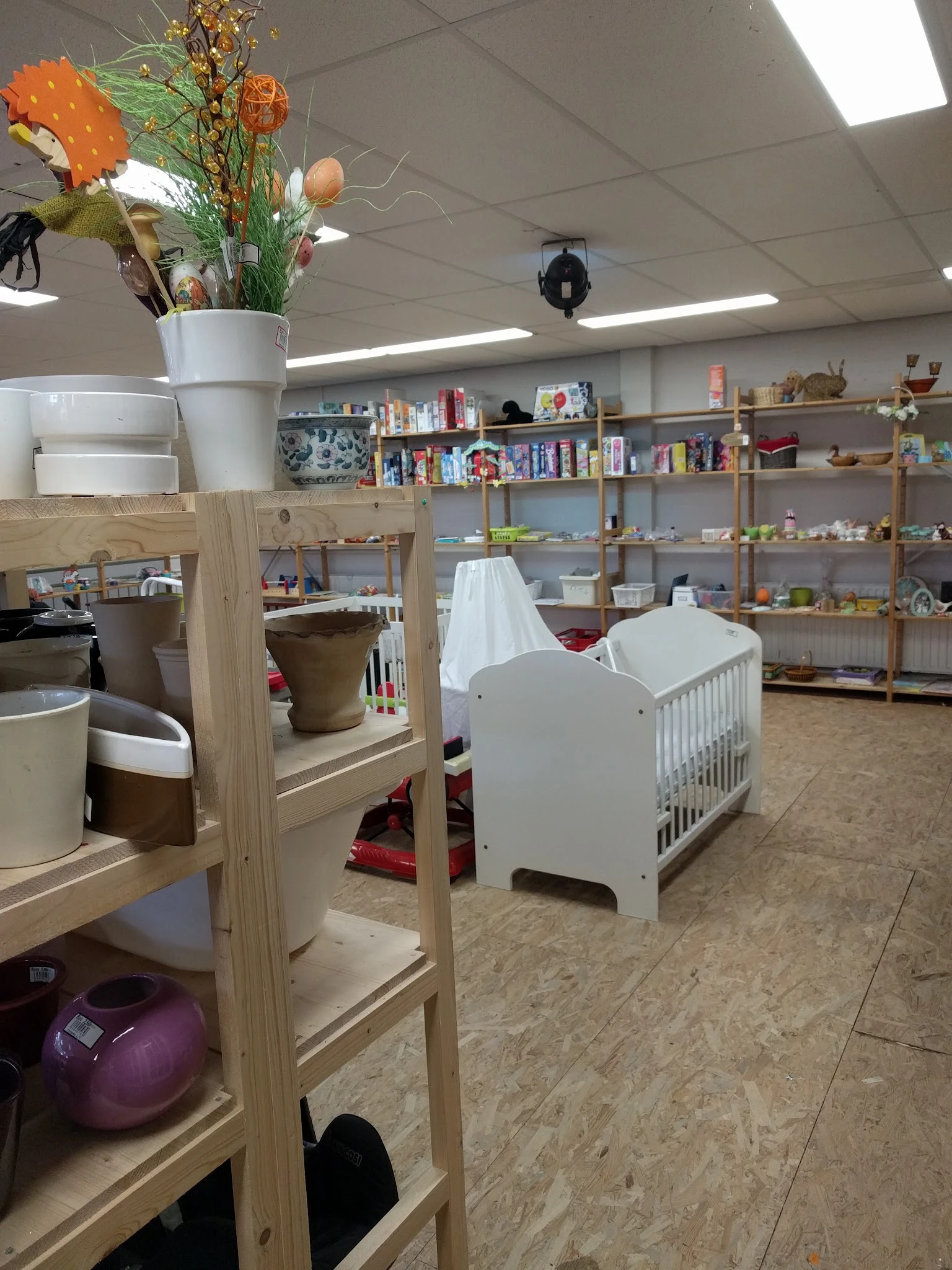 Winkelvloer met houten stellingen, babykribben, boeken, speelgoed en huishoudartikelen