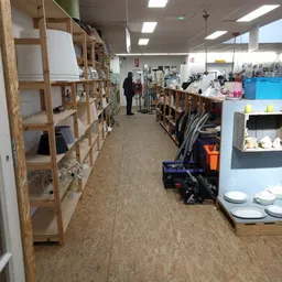 Winkelinterieur met houten stellingen vol spullen aan beide zijden van een gang, klant loopt verder weg