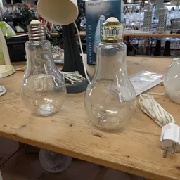 Twee glazen lampenkappen in vorm van gloeilampen op houten tafel
