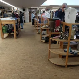Winkelvloer van kringloopwinkel met houten displaykasten en uiteenlopende tweedehands spullen, bezoekers in het achtergronд