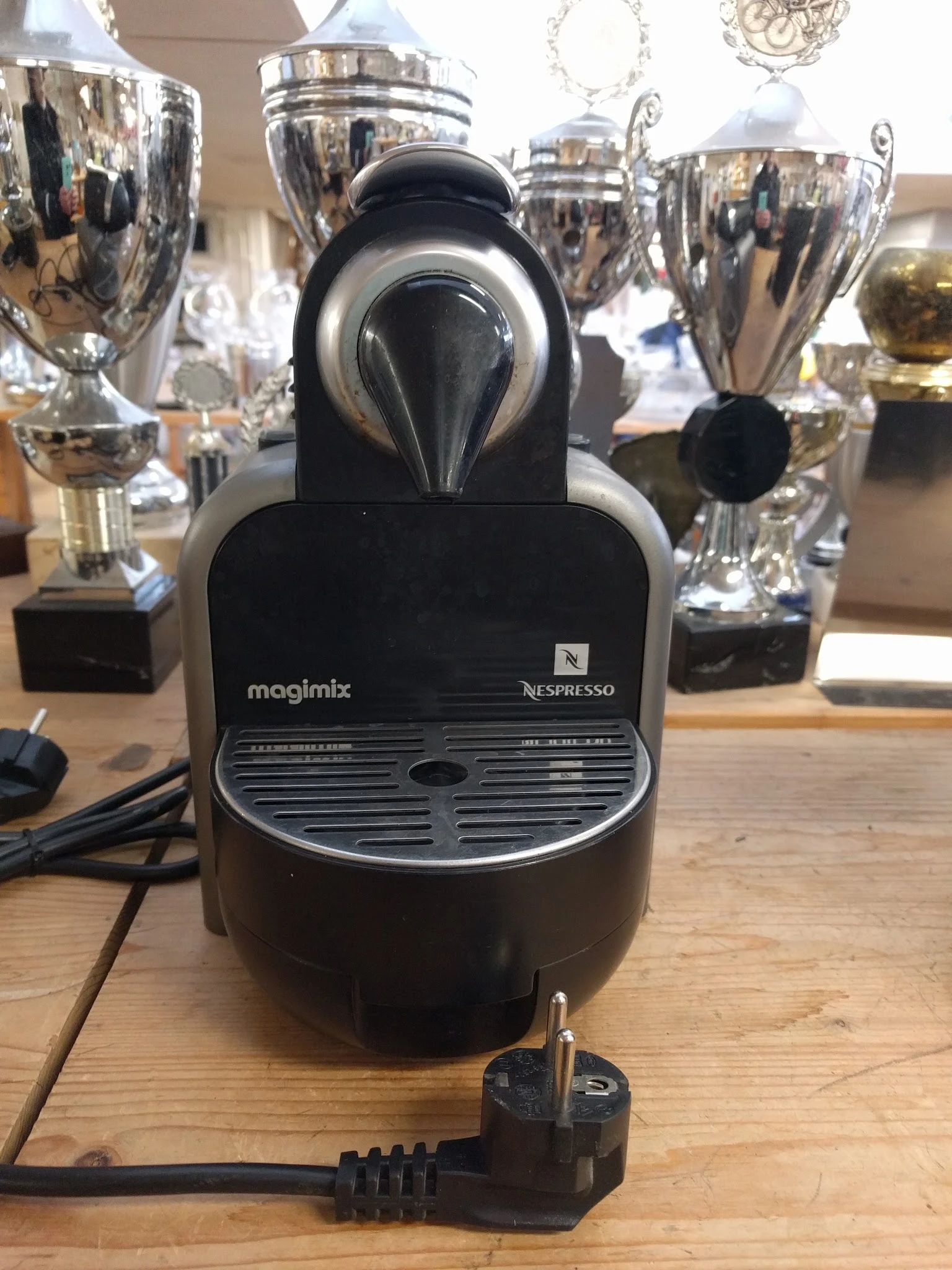 Magimix Nespresso koffieapparaat in zwart, close-up van het apparaat met tropheeën op de achtergrond