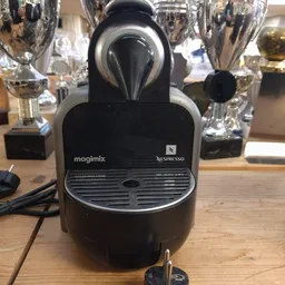 Magimix Nespresso koffieapparaat in zwart, close-up van het apparaat met tropheeën op de achtergrond