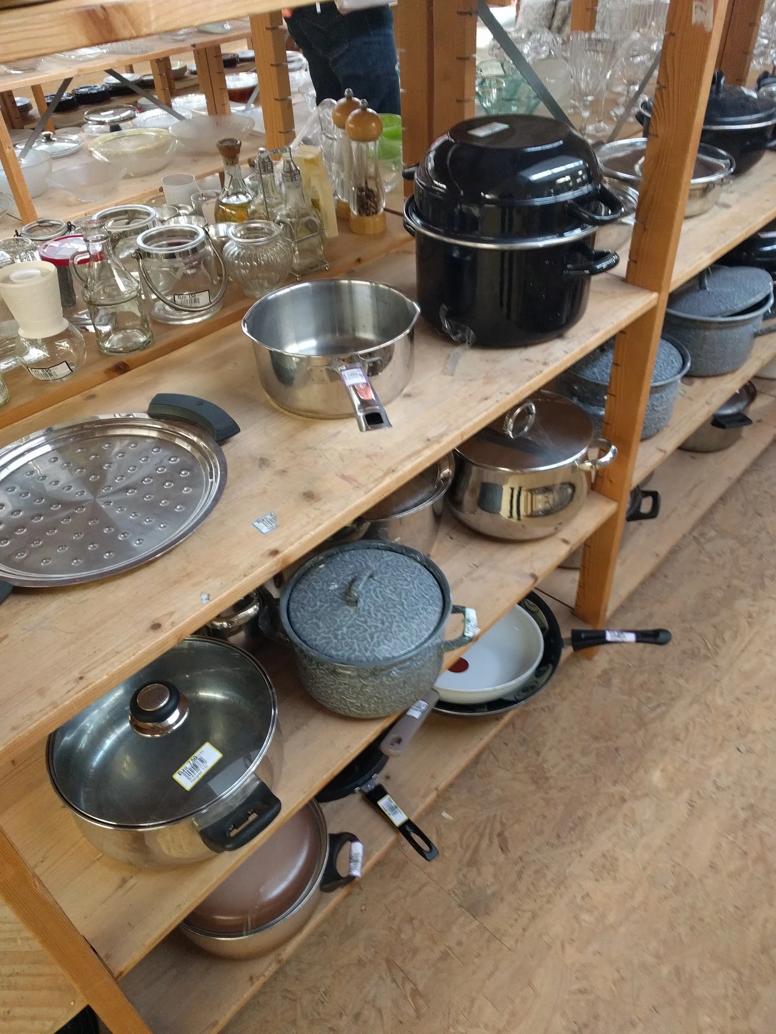 Diverse kookgerei en pannen op houten toonbank, waaronder steelpannen, zeef en deksel.