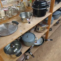 Diverse kookgerei en pannen op houten toonbank, waaronder steelpannen, zeef en deksel.