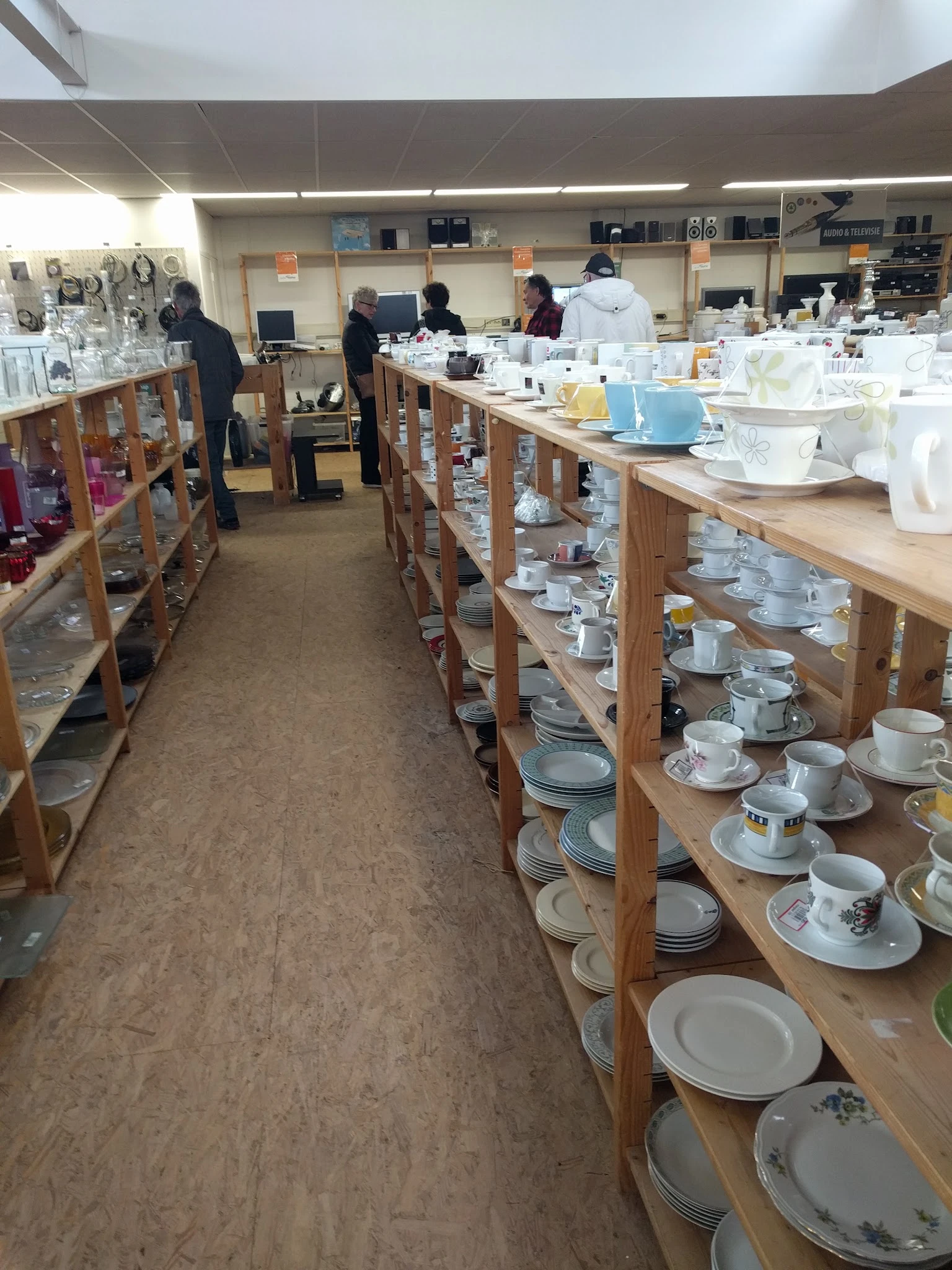 Houten stellingen met uitgestalde serviesgoed, kopjes, schotels en ander keramiek in de kringloopwinkel