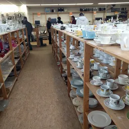 Houten stellingen met uitgestalde serviesgoed, kopjes, schotels en ander keramiek in de kringloopwinkel