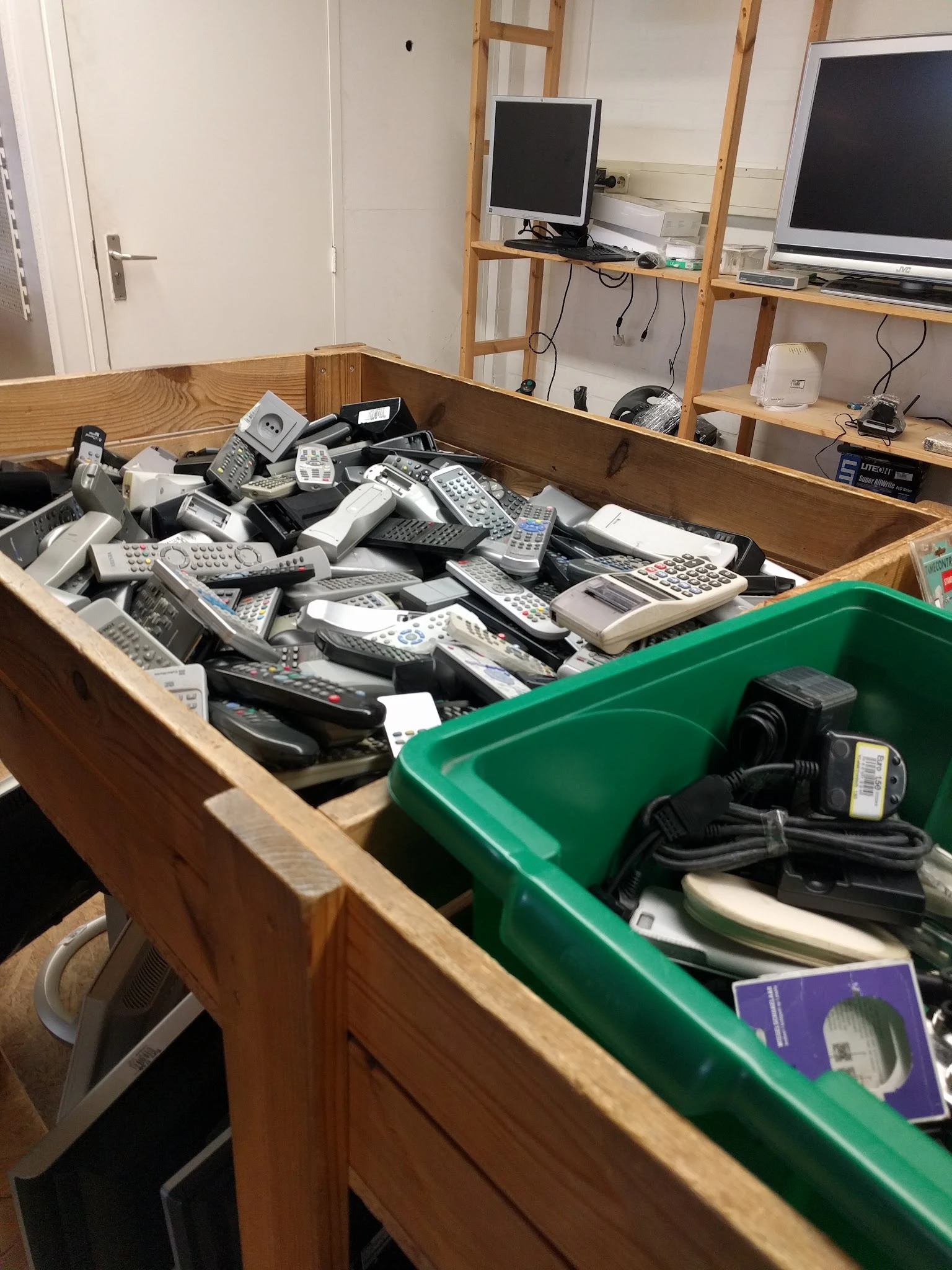 Houten en groene plastic bakken vol met gebruikte telefoons, afstandsbedieningen en elektronische apparaten