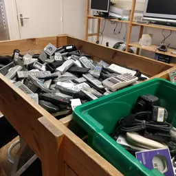 Houten en groene plastic bakken vol met gebruikte telefoons, afstandsbedieningen en elektronische apparaten