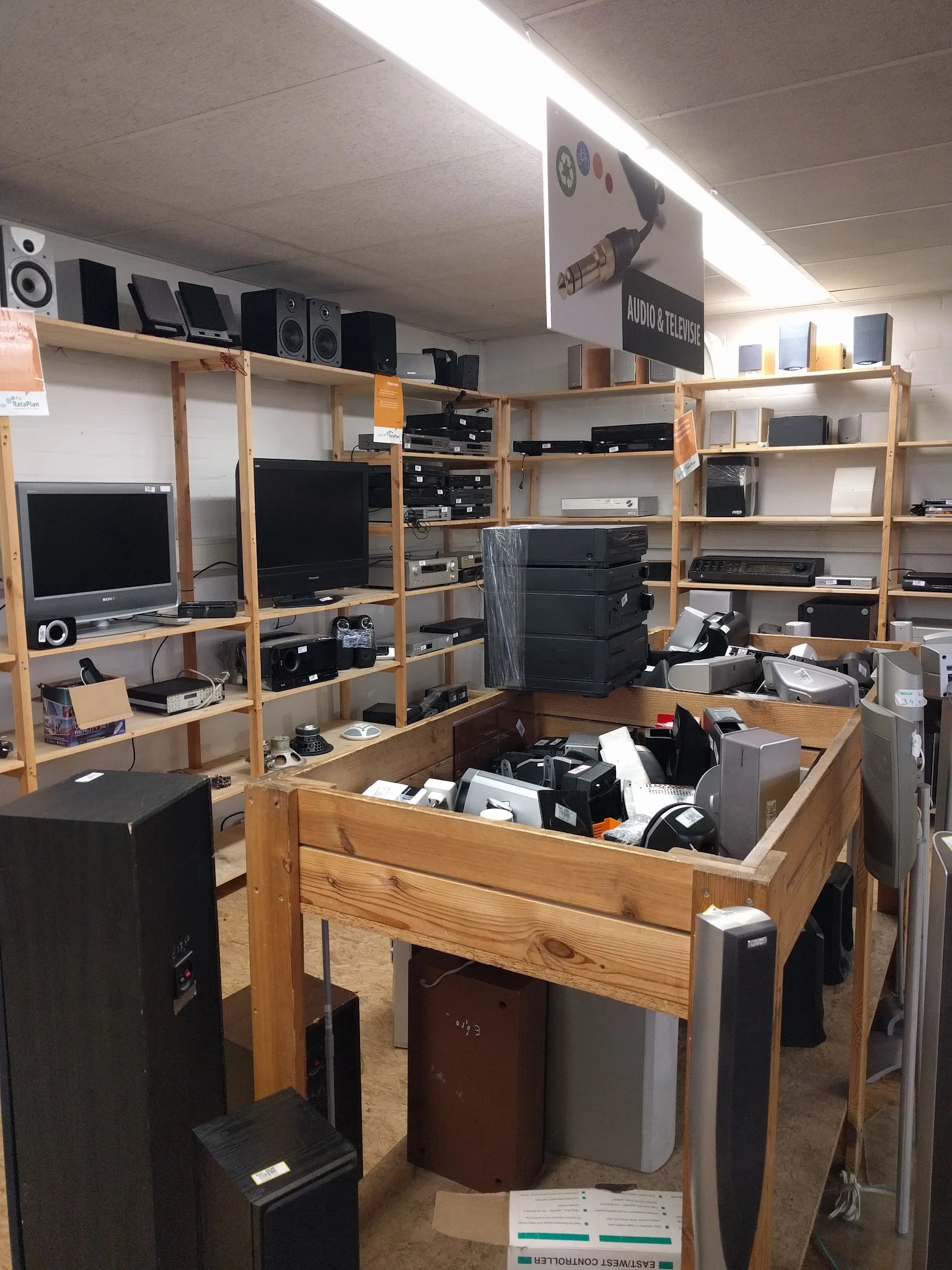 Houten stellingen met elektronische apparatuur en onderdelen in een kringloopwinkel