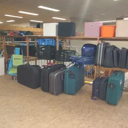 Uitgestalde koffers en tassen in verschillende kleuren en maten op de kringloopwinkelsvloer