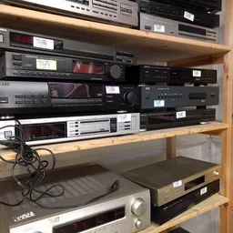 Tweedehands elektronische apparatuur in een stellingkast: versterkers, tuners en andere audio-equipement