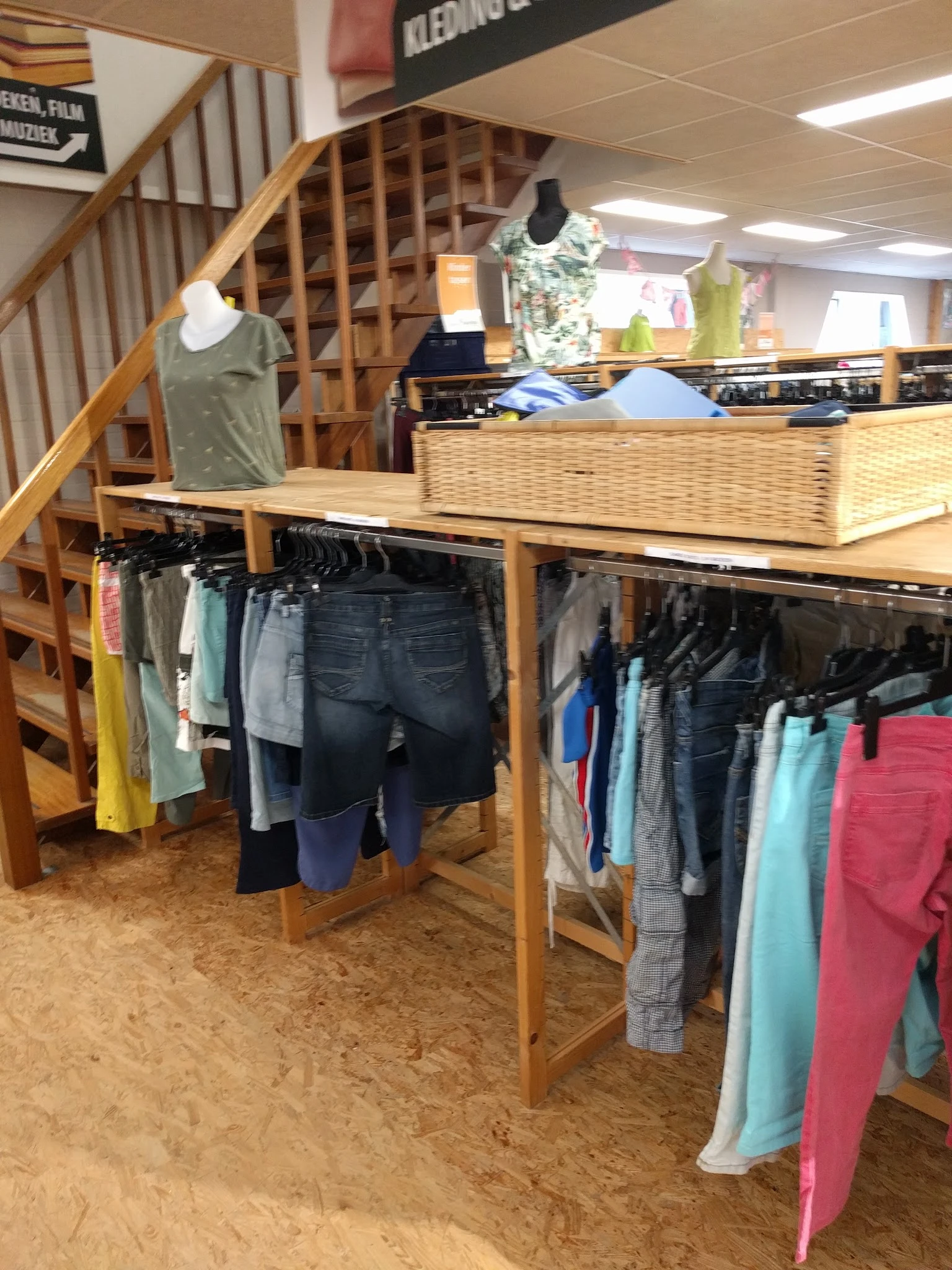 Houten stellingen met tweedehands kleding op hangers en een rieten mand boven