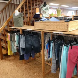 Houten stellingen met tweedehands kleding op hangers en een rieten mand boven