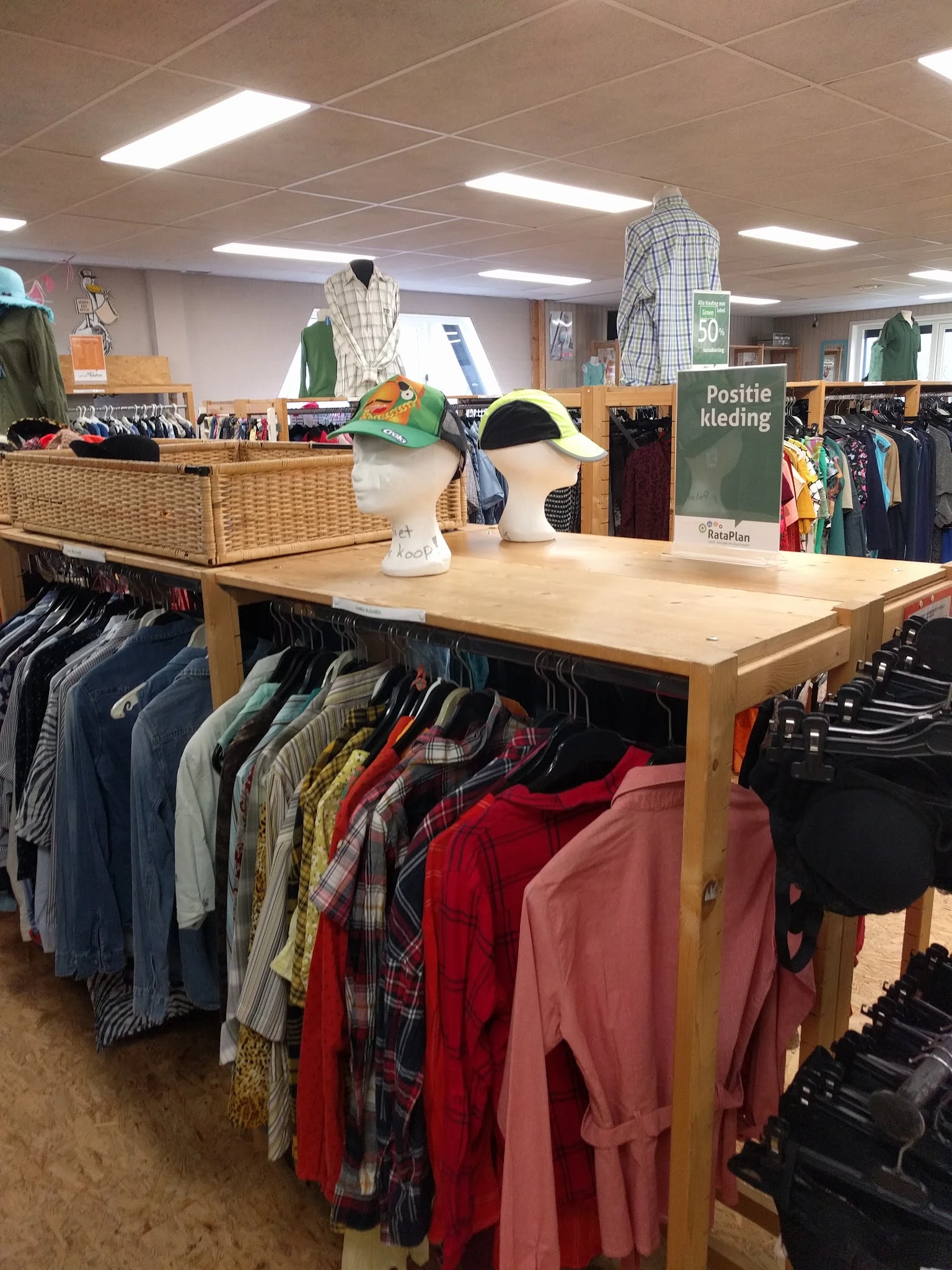 Kledingafdeling met houten toonbank, kledingrekken met diverse jassen en kleding, en een bordje 'Positie kleding'