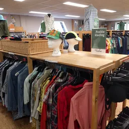 Kledingafdeling met houten toonbank, kledingrekken met diverse jassen en kleding, en een bordje 'Positie kleding'