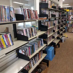 Stellingen met dvd's en blu-rays in een kringloopwinkel, met zwarte opbergbakken en een blauwe prullenbak