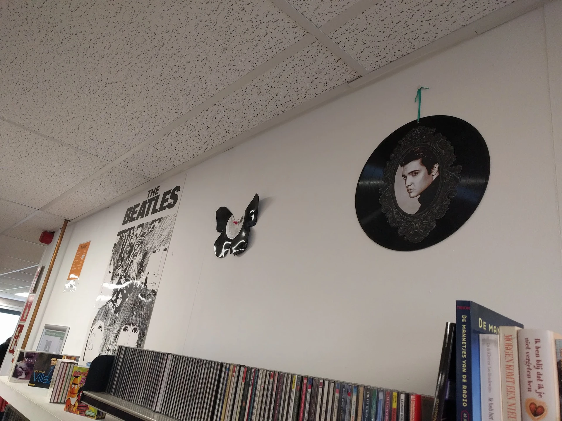 Witmuur met The Beatles-poster, vinyl record artwork en CD-collectie op plank