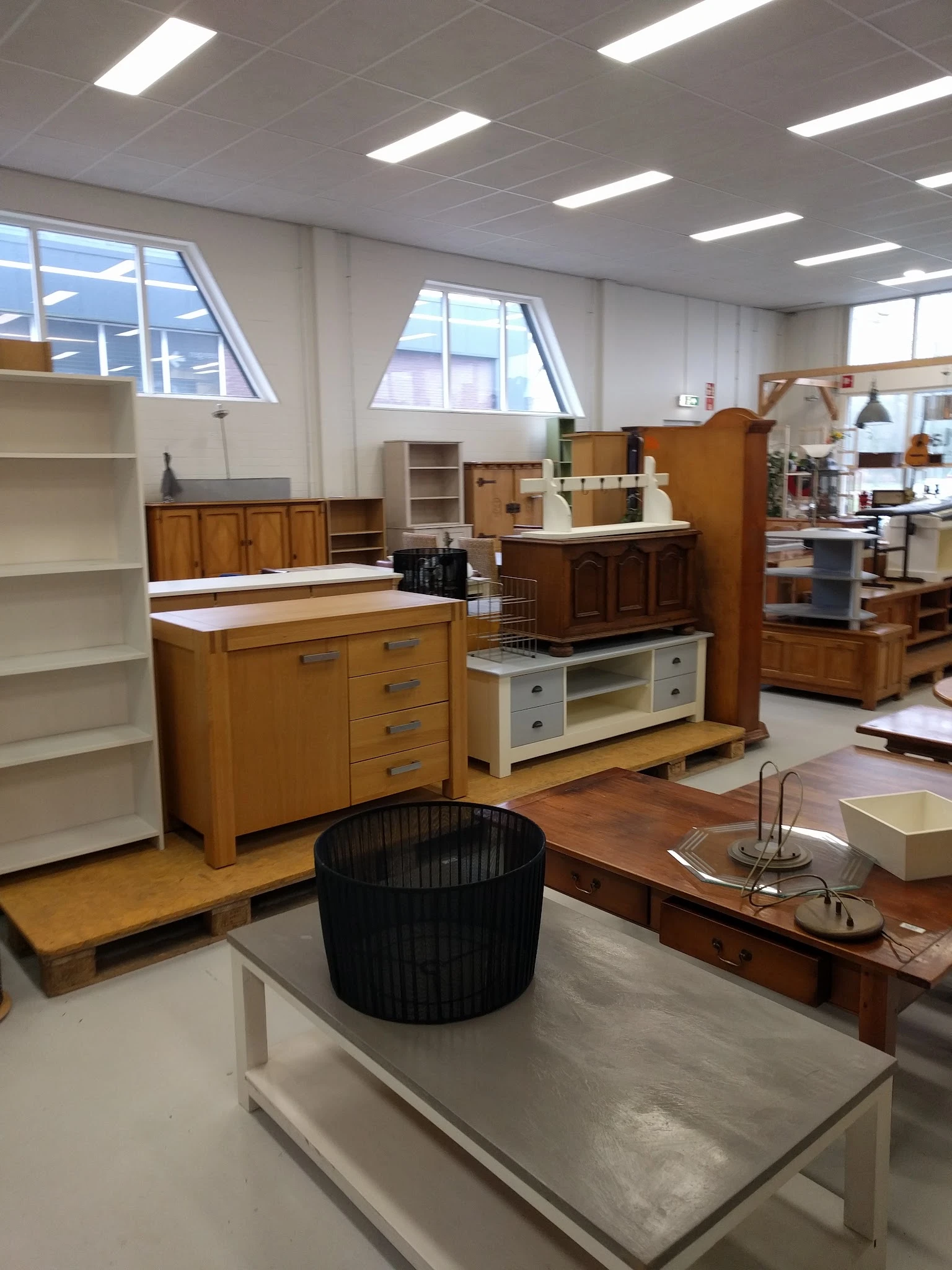 Kringloopwinkel met uitgestalde meubels: houten kasten, tv-meubel, boekenkast en zwarte stoel