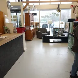 Winkelvloer van kringloopwinkel met stellingen, meubels en toonbanken, zicht op ingang met ramen