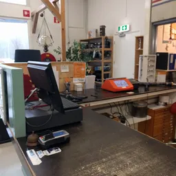 Binnenzicht van kringloopwinkel met werkplek, monitoren, kasten en diverse spullen op tafels