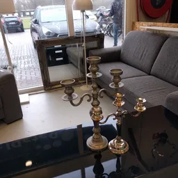 Twee gouden kandelaars met meerdere armen op een witte tafel in de winkel