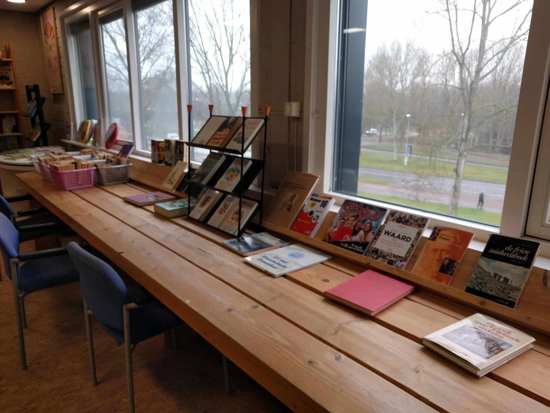 Houten toonbank met uitgestalde boeken en voorwerpen voor verkoop, grote ramen met uitzicht op park
