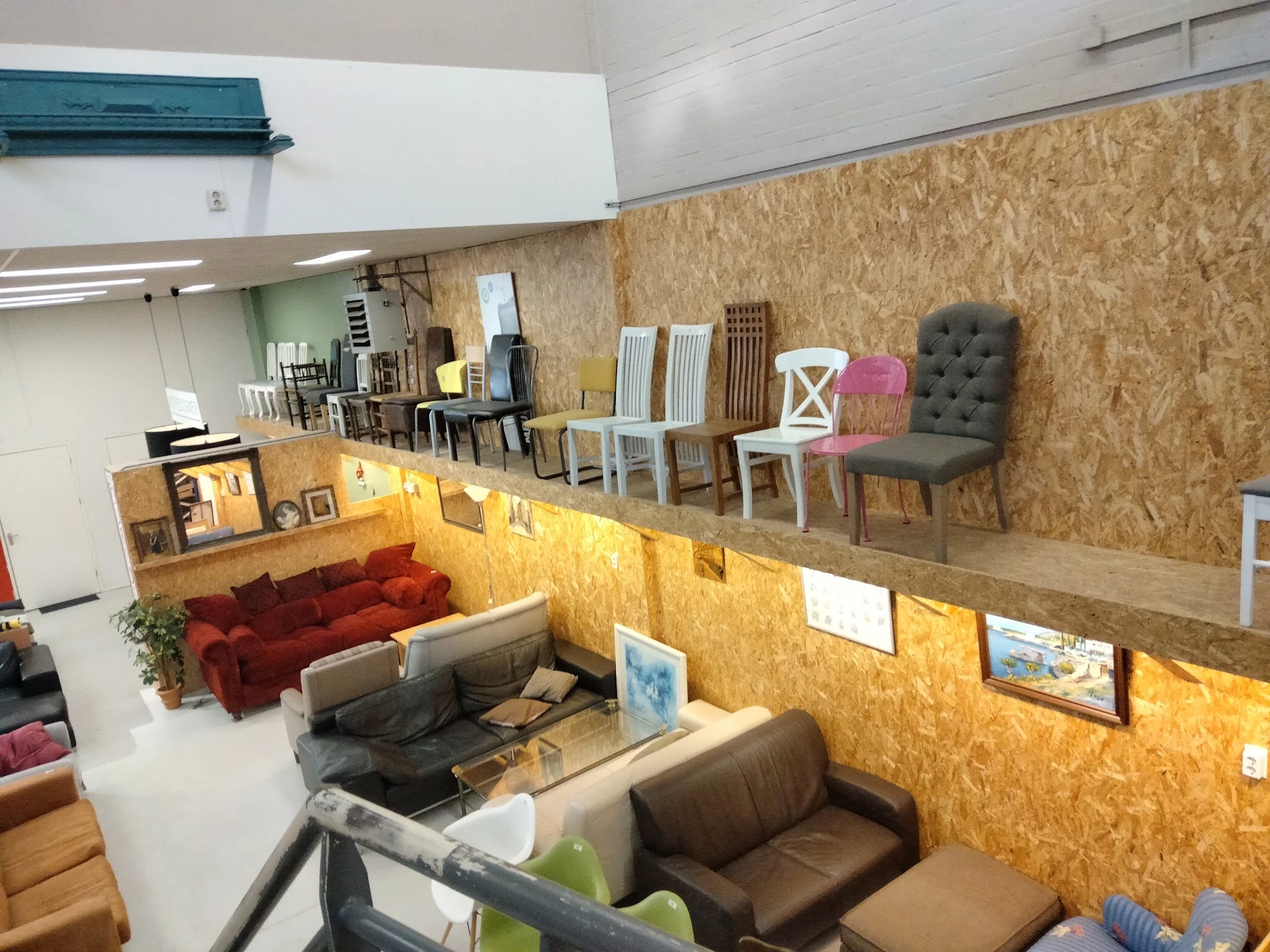 Winkelvloer met uitgestalde meubels: rode bank, bruine fauteuils, stoelen en decorstukken tegen kurken wand
