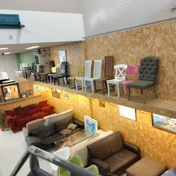Winkelvloer met uitgestalde meubels: rode bank, bruine fauteuils, stoelen en decorstukken tegen kurken wand