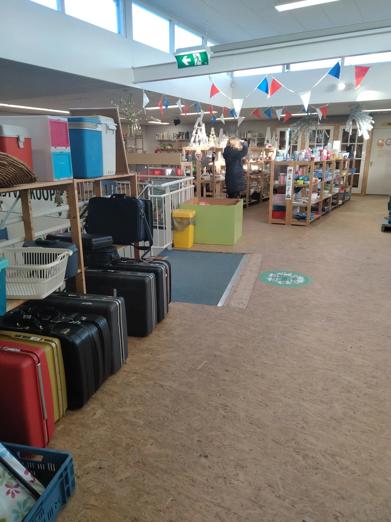 Winkelvloer met koffers, stellingen met spullen en verschillende afdelingen in de kringloopwinkel