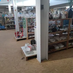 Winkelvloer van kringloopwinkel met stellingen vol servies, glazen en huishoudartikelen, witte zuilen, aardewerk vloer