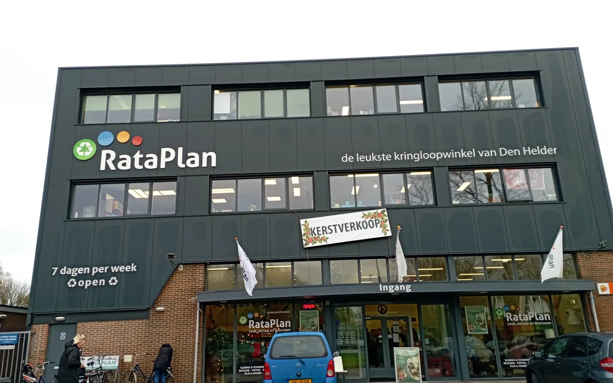 Gevel van kringloopwinkel RataPlan met grote ramen, groene gevelbekleding en duidelijk zichtbaar logo en winkelnaam