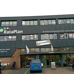 Gevel van kringloopwinkel RataPlan met grote ramen, groene gevelbekleding en duidelijk zichtbaar logo en winkelnaam